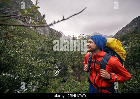 Portrait of happy tourist with big backpack is in the mountain valley of Karakol national park, Kyrgyzstan Stock Photo