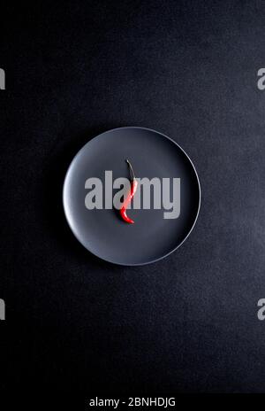 Minimalist composition of red chili pepper in black ceramic plate at black table Stock Photo