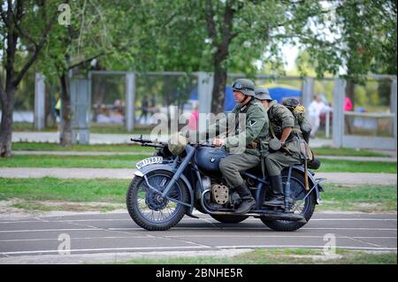 Reenactors dressed in uniform of German soldier of World War II riding an old military motorcycle in a park Stock Photo