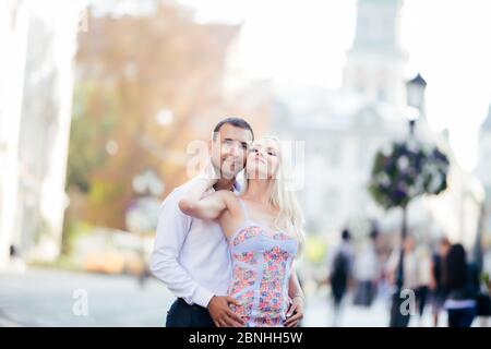 Lovely couple walking around the block. Dark-haired man in a white shirt hugging a blonde in a beautiful dress Stock Photo