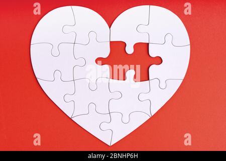 Love, charity, donation, helping concept. Missing piece of jigsaw puzzle in heart shape on red. Looking for love partner. Uncompleted puzzle. Relation Stock Photo