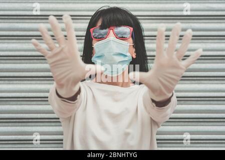 woman wearing medical mask for coronavirus with sunglasses spreading hands up outdoor Stock Photo