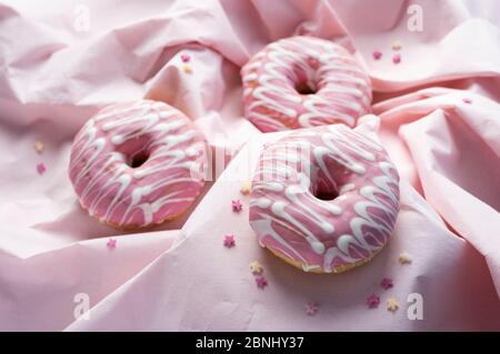 Pink glaze decorated donuts on wavy pink background in various focus Stock Photo