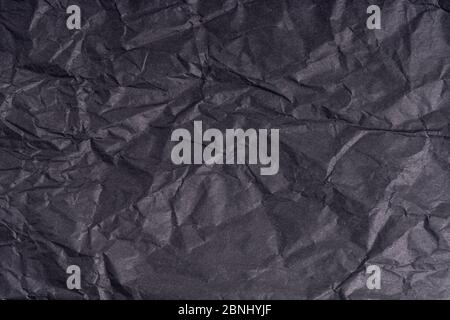 Dark wrinkled creased black paper poster texture. Blank creased crumpled grainy paper textured surface. Smudged grungy cardboard with fiber. Close up. Stock Photo