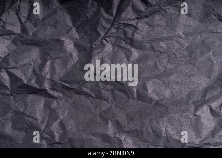 Dark wrinkled creased black paper poster texture. Blank crumpled grainy paper textured surface. Smudged grungy cardboard with fiber. Close up. Materia Stock Photo