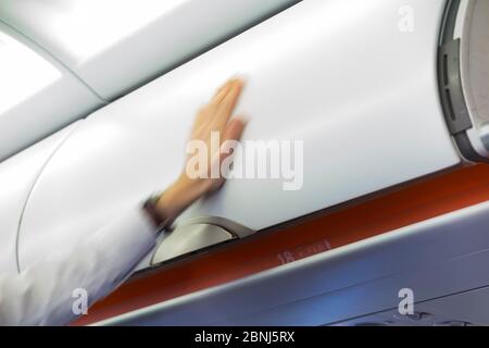Flight attendant member of cabin crew closes airplane air plane overhead luggage bin / locker / lockers / compartment / compartments door containing passengers hand bags. (115) Stock Photo