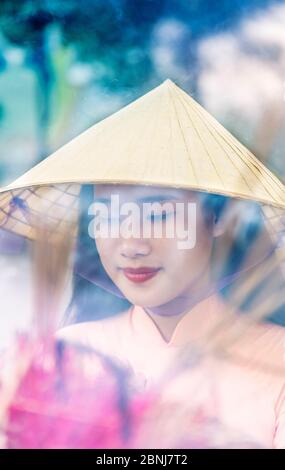 A young Vietnamese woman in a conical hat making incense offerings at a Buddhist temple, Hue, Vietnam, Indochina, Southeast Asia, Asia Stock Photo