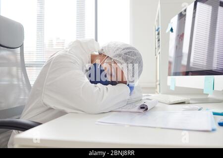 Exhausted female doctor in protective glasses and mask sleeping at the table she tired of hard work at hospital Stock Photo