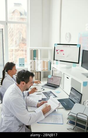 Two doctors sitting at the table and making notes in documents together during their work at office Stock Photo