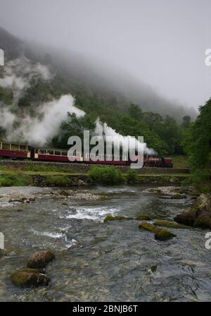 A steam train enters Aberglaslyn Pass, alongside the river Glaslyn, near Beddgelert, Wales, UK June Stock Photo