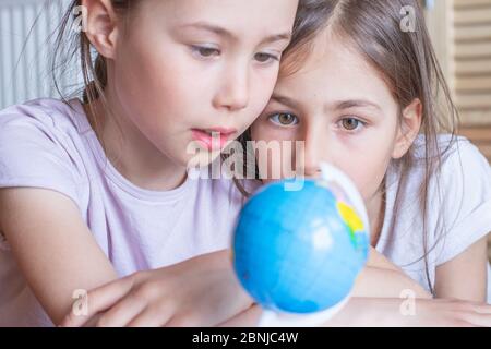 Child girl are sitting at home and looking at the globe, dreaming about traveling around the world. Stock Photo