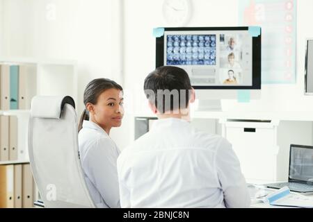 Two doctors talking to each other while sitting at the table and examining x-ray images at office Stock Photo