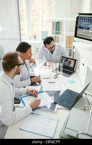 Group of doctors sitting at the table and talking to their colleague during online conference at meeting Stock Photo