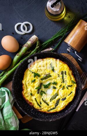 Healthy Asparagus Omelet. Egg omelet with asparagus and onions in a cast iron skillet on a stone countertop. Top view flat lay background. Stock Photo