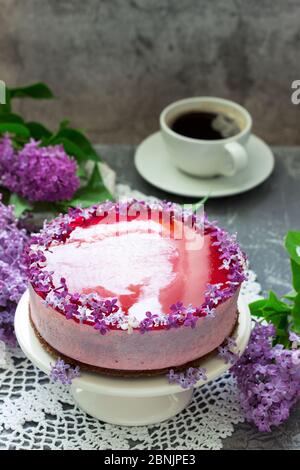 A berry mousse cake with chocolate base and juice jelly, decorated with lilac flowers, served with coffee. Stock Photo