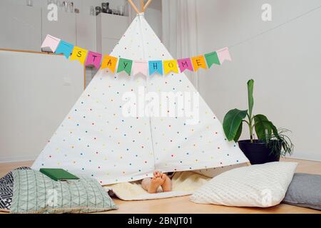 Feet sticking out from under a hut with stay at home garland Stock Photo