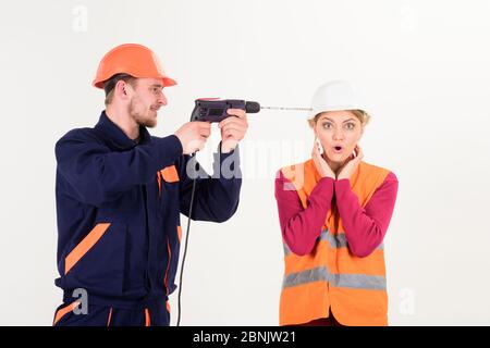 Man with happy face drills head of woman, white background. Builder, repairman makes hole in female head. Woman with shocked face in helmet, hard hat. Husband annoying his wife. Headache concept. Stock Photo