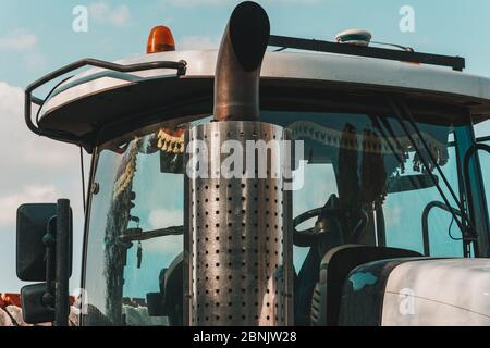 Catalytic converter tractor and cab with large windows close up on a background of blue sky. Exhaust pipe of a modern new bulldozer. Stock Photo