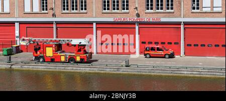 Red fire engine truck and service car parked in front the main entrance of a 'Sapeurs Pompiers' fire station along the Canal Saint-Martin. Stock Photo