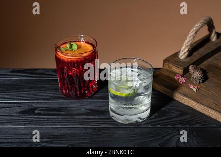 Two coctails on a wooden table near a tray, one Negroni other Caipirinha, traditional Brazilian alcoholic drink, typical drink made with sugar, lemon Stock Photo