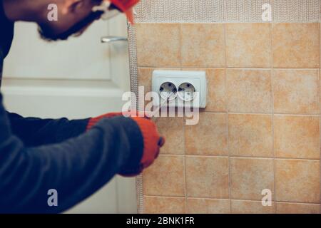 Electrician repair a wall socket at home or office. Closeup of man in workwear repairing an electrical outlet. Hazardous concept, high voltage, risk, wiring replacement, technician's occupation. Stock Photo