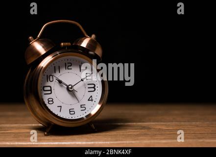 Vintage alarm clock classic with bell brown color on a wood table and black background close-up clock to the left Stock Photo
