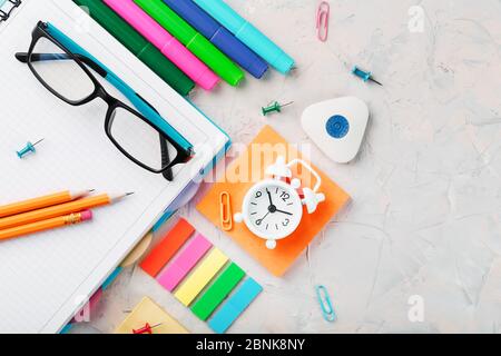 Office supplies lie on a gray table, for working with your own hands at home. The color of the rainbow, pencils, glasses, Notepad and alarm clock remi