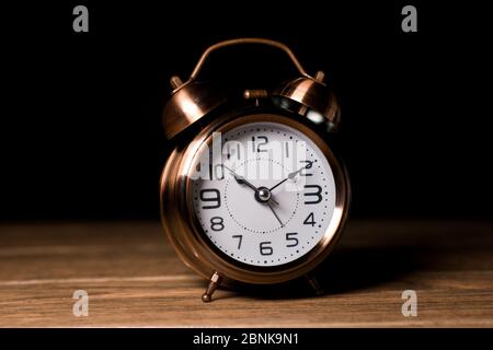 Vintage alarm clock with bell brown color metallic close-up with in midnight wooden table and black background Stock Photo