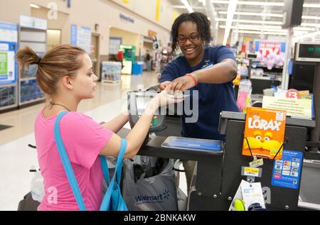 San Marcos Texas USA, 2012: Smiling African-American female cashier gives cash change to young White female customer at a Wal-Mart Supercenter. ©Marjorie Kamys Cotera/Daemmrich Photos Stock Photo