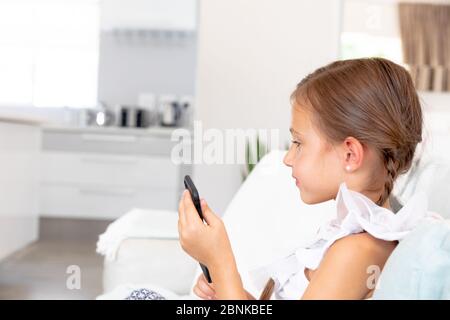Caucasian girl sitting on a couch and using her smartphone Stock Photo