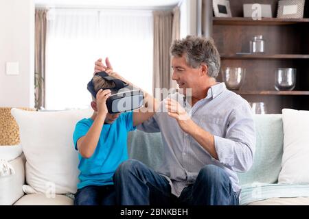 Senior Caucasian man using a VR headset at home with his grandson Stock Photo