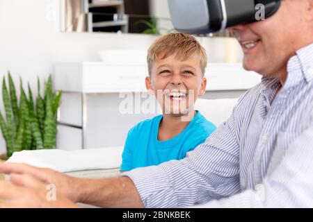 Senior Caucasian man using a VR headset at home with his grandson Stock Photo