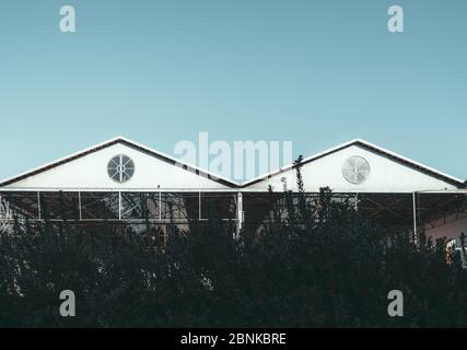 An outdoor view of two triangle metal roofs with a single round window in each one of metro or train depot buildings, outdoor storage facilities, or h Stock Photo