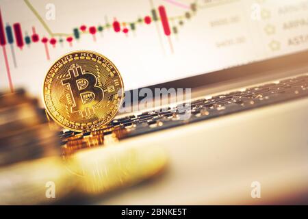 Golden Bitcoin Leaning On Laptop Keyboard With Performance Graphs On Computer Screen. Stock Photo