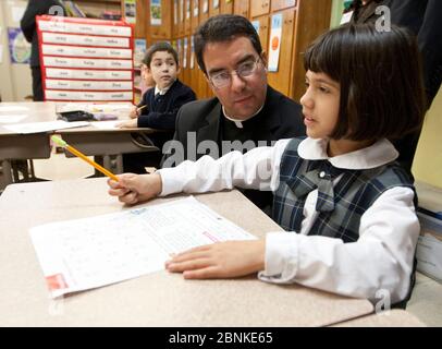 Catholic bishop wearing the traditional clerical collar speaks with second grade female student while visiting the classroom at private religious school. ©Bob Daemmrich Stock Photo