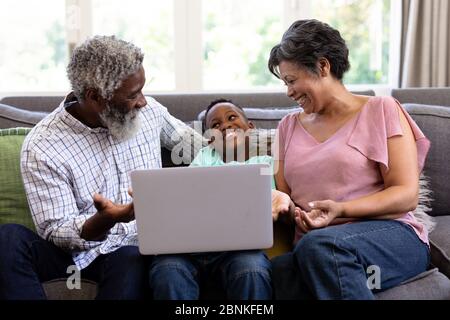 Mixed race boy and his grandparents using a laptop sitting on a couch Stock Photo