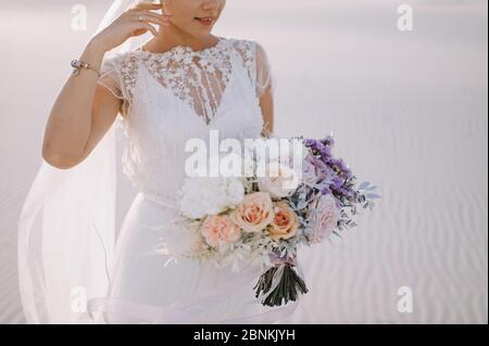 Close-up of a bride’s bouquet of roses, carnations in white, pink, violet, lavender, peach shades. The bride in a lace white dress holds a bouquet Stock Photo