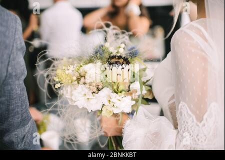 Close-up of a bride’s bouquet of white flowers and protea. The bride in a lace white dress holds a bouquet in her hands Stock Photo