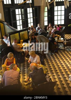 dh Long bar RAFFLES HOTEL SINGAPORE Tourist people relaxing with drinks at tables hotels colonial pub Stock Photo