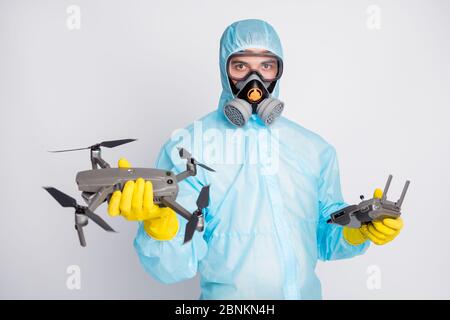 Portrait of man hold robot airplane drone joystick wear white hazmat suit yellow rubber gloves goggles breathing mask isolated over blue color Stock Photo