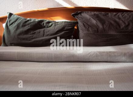 Bed linen detail with sunlight and shadows on white cotton blanket and dark grey pillows Stock Photo