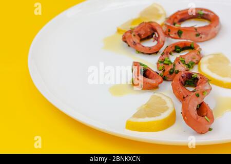 Fresh squid grill sliced with lemon, calamari rings on white plate on yellow background. Selective focus. Stock Photo