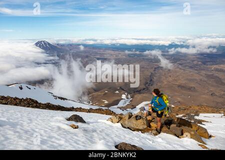 A female climber standing on the slopes of Mount Ruapehu and looking out towards Mount Ngauruhoe, Tongariro National Park, New Zealand Stock Photo