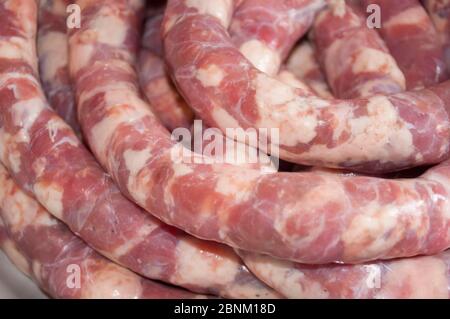 Making homemade sausage at home. Stuffing pork intestine with meat and fat. The photo shows the stage when the already stuffed raw sausage is rolled i Stock Photo