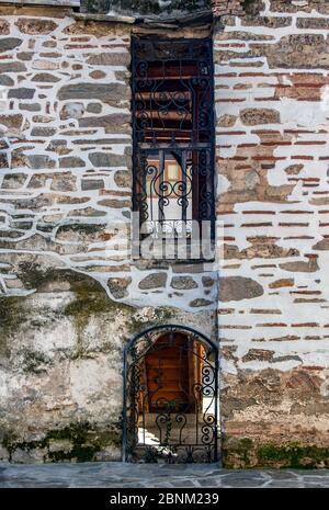 Medieval monastery wall with a door and a window with wrought iron ornaments. Stock Photo
