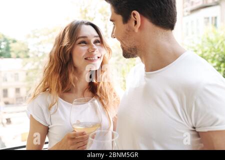 Image of caucasian young couple smiling while holding glasses and drinking wine together on balcony outdoors Stock Photo
