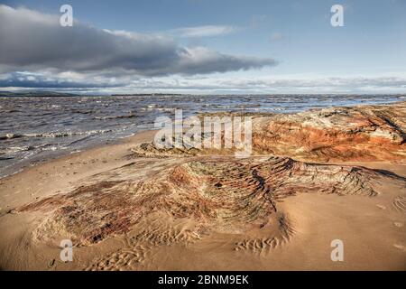 Sandstone rocks eroded by tidal action at high tide near Hilbre Point,  Hilbre Island and North Wales in the background at high tide Dee Estuary Hoyla Stock Photo