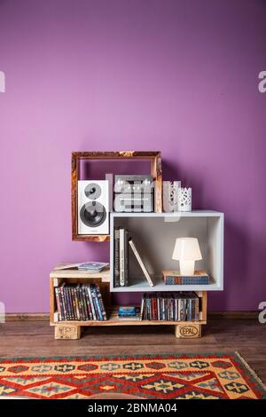 Construction of a shelf made of wood, Euro pallet, solid wood, MDF board; Do-it-yourself production step-by-step, final photo 01 in the living room in front of a purple wall on a wooden floor Stock Photo