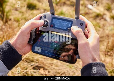 Close up mans hands holding drone remote controller with smartphone in the field. Concept of aerial shooting and flying, San Francisco, May 2020. Stock Photo