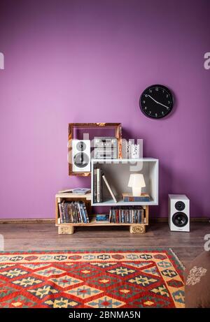 Construction of a shelf made of wood, Euro pallet, solid wood, MDF board; Do-it-yourself production step-by-step, final photo 02 in the living room in front of a purple wall on a wooden floor Stock Photo